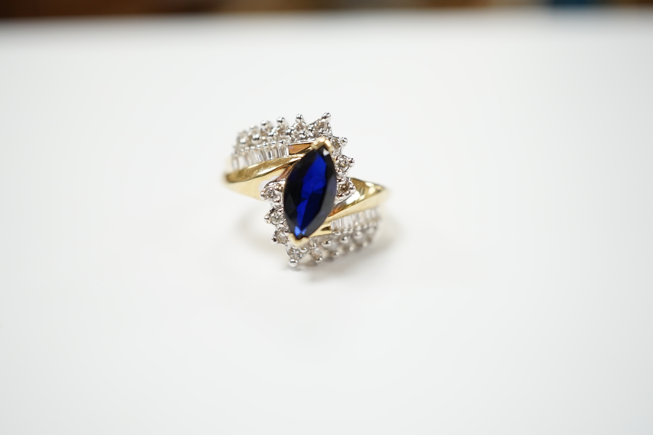A modern 14k and single stone marquise cut sapphire and diamond chip cluster set crossover dress ring, size M, gross weight 5.3 grams.